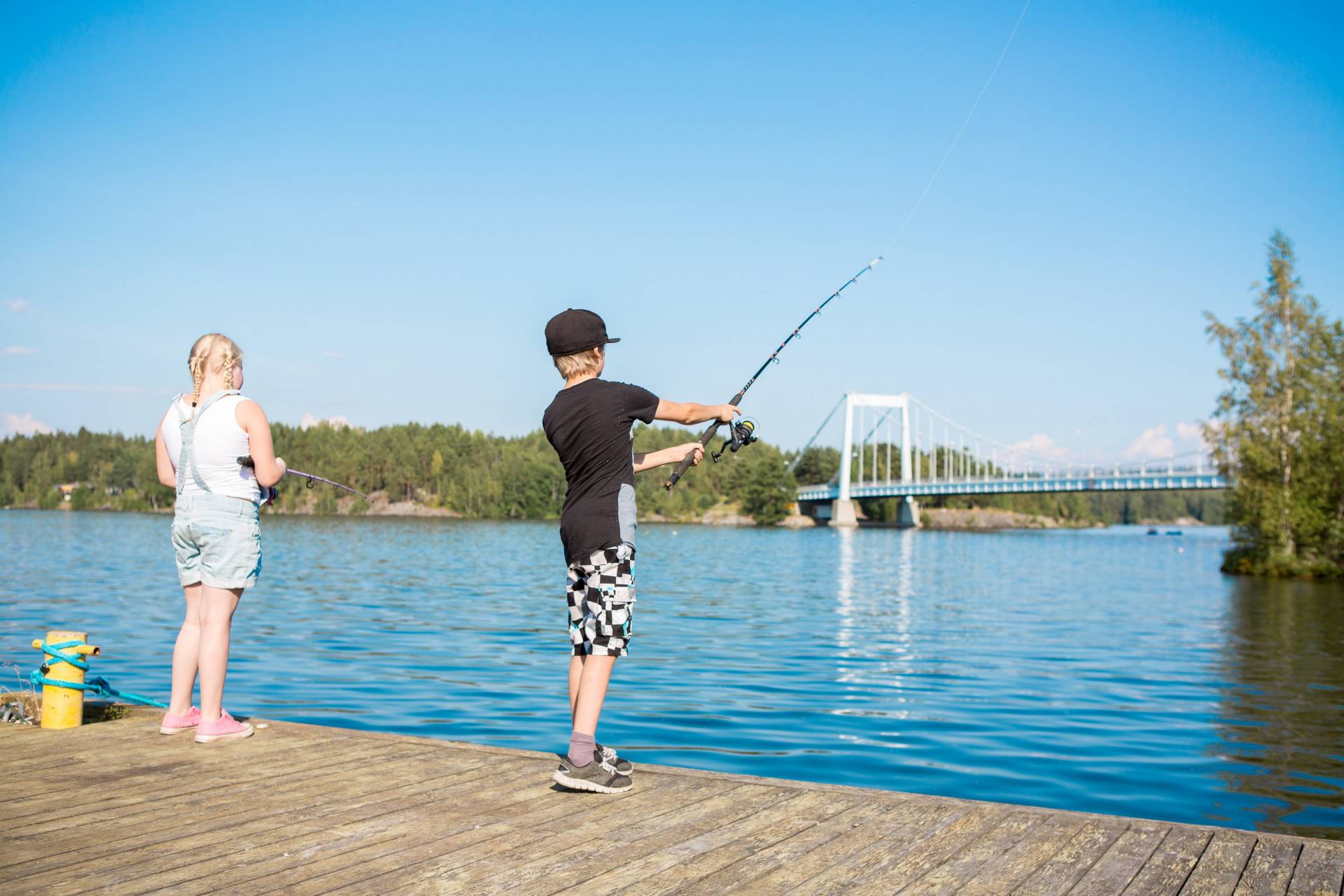 Tyttö ja poika kalastavat laiturilla