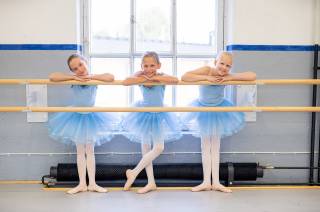 kolme balettitanssijaa seisovat hymyillen ikkunan vieressä.