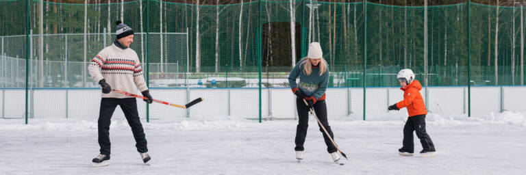 Perhe pelaamassa jääkiekkoa Kerhomajan kentällä.