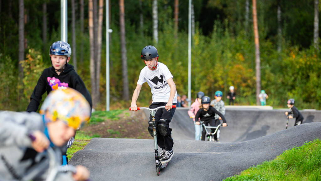 Lapsia Walklandian pumptrack-radalla scoottaamassa ja pyöräilemässä.